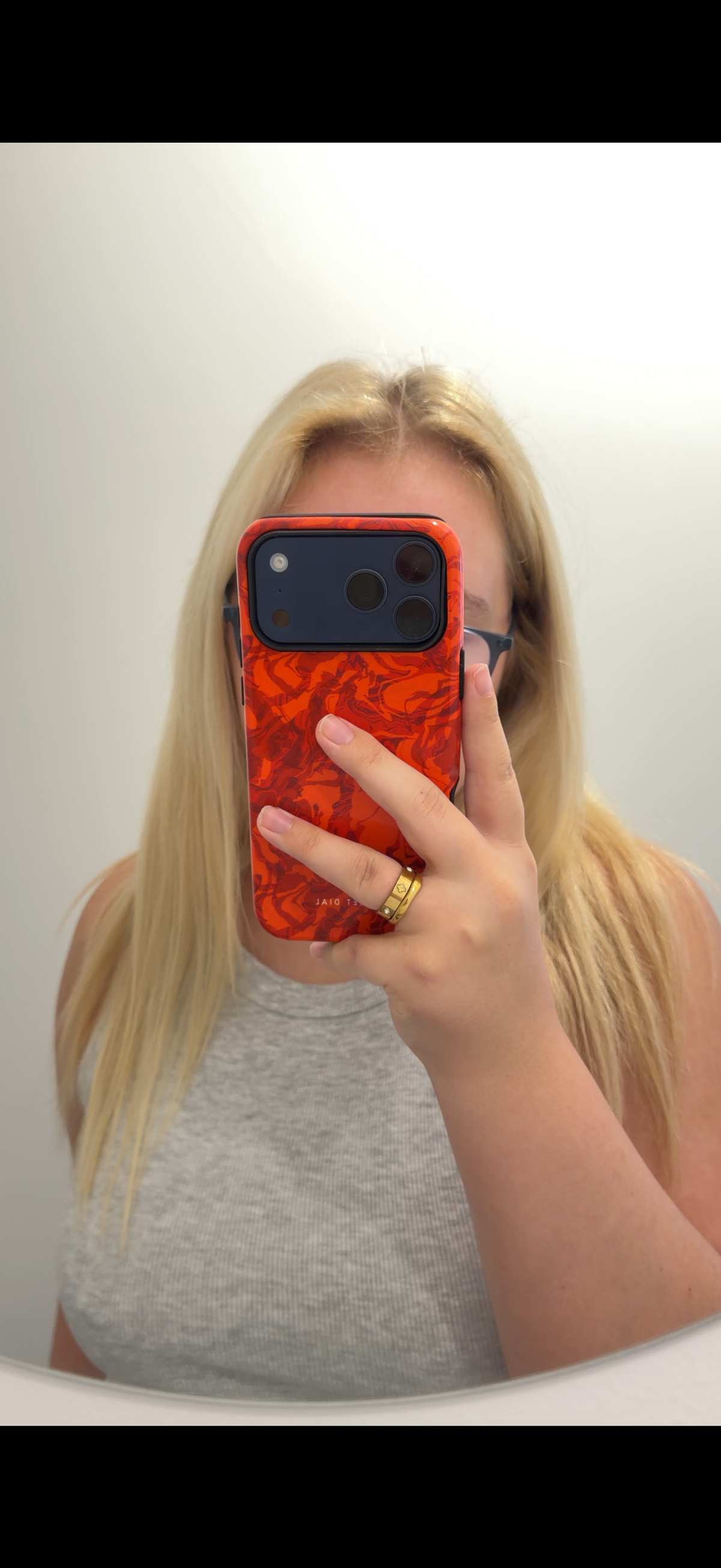 Woman taking a mirror selfie with an orange patterned case, on a blue iPhone pro max
